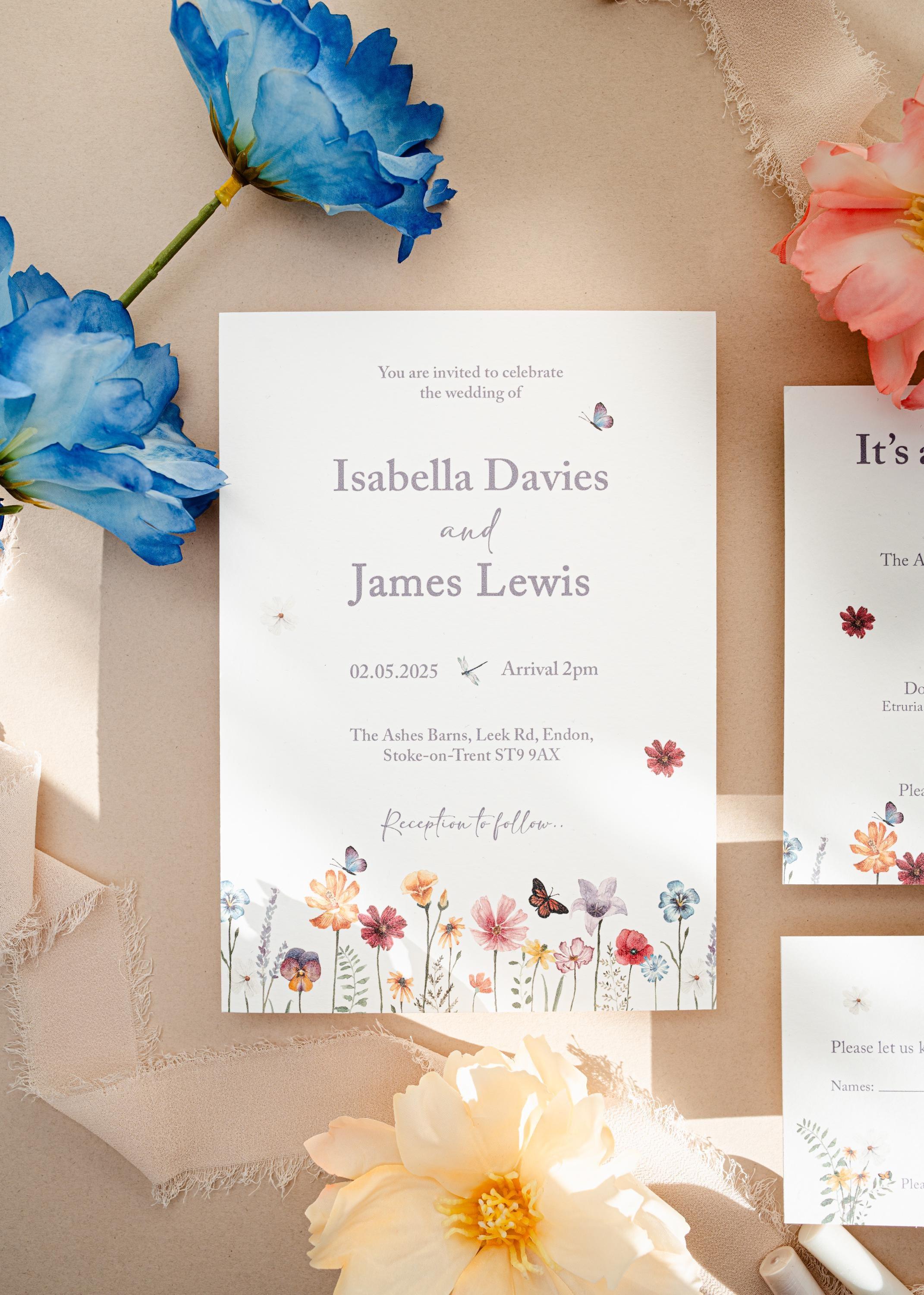 Close-up of a watercolour wildflower wedding invitation for Isabella Davies and James Lewis, showing the painted flowers, butterflies and a dragonfly in natural sunlight