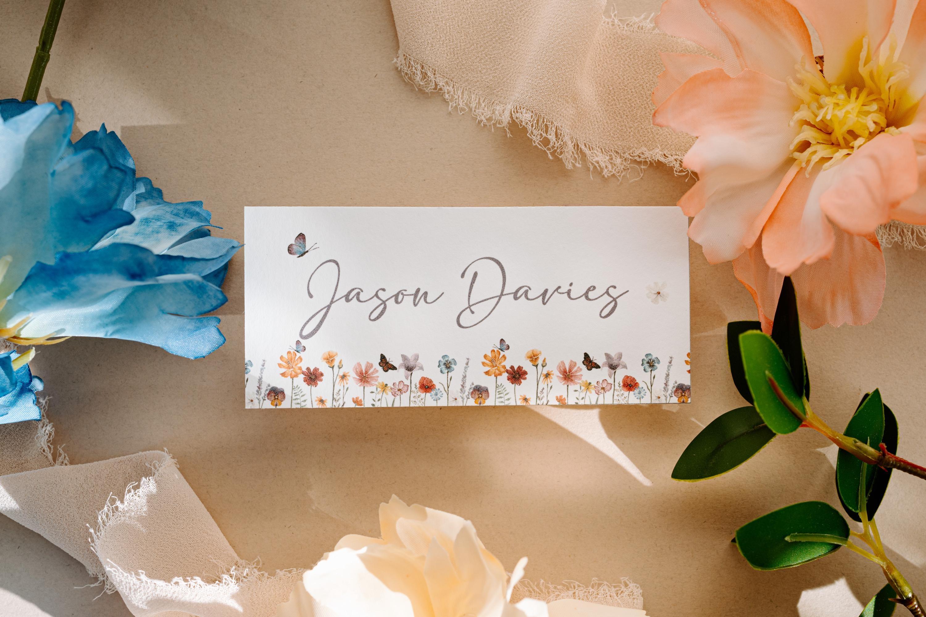Wildflower wedding place card with a floral border and the name Jason Davies in cursive script, surrounded by blue, pink and white flowers
