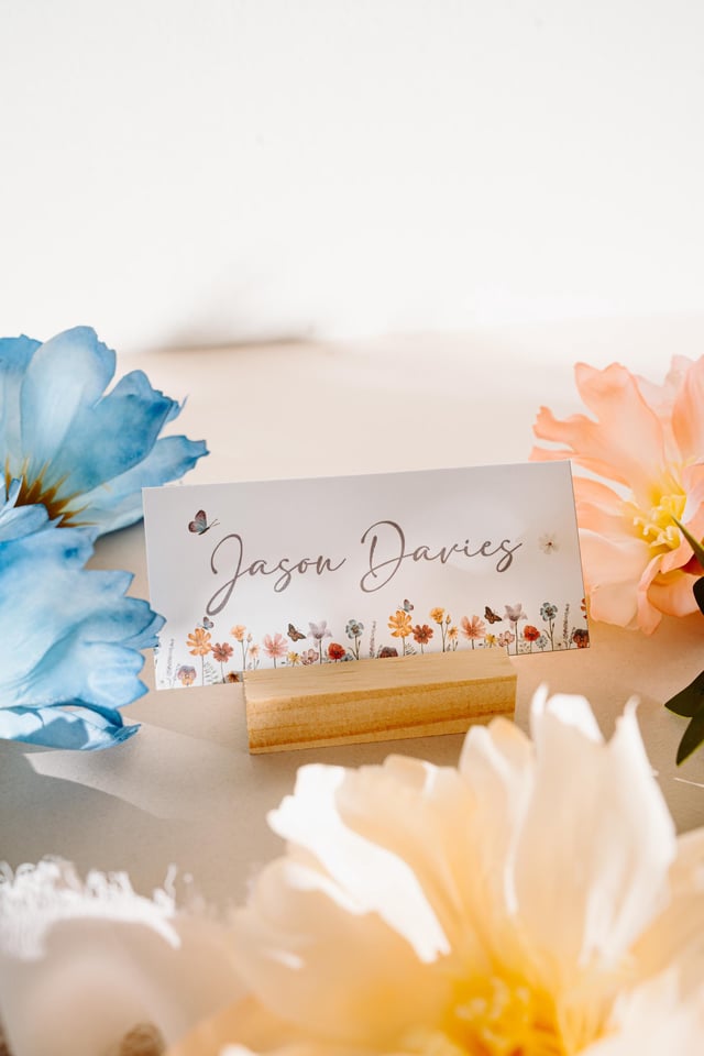 A white card with a floral border and the name "Jason Davies" written in cursive. The card is sitting on a small wooden stand.