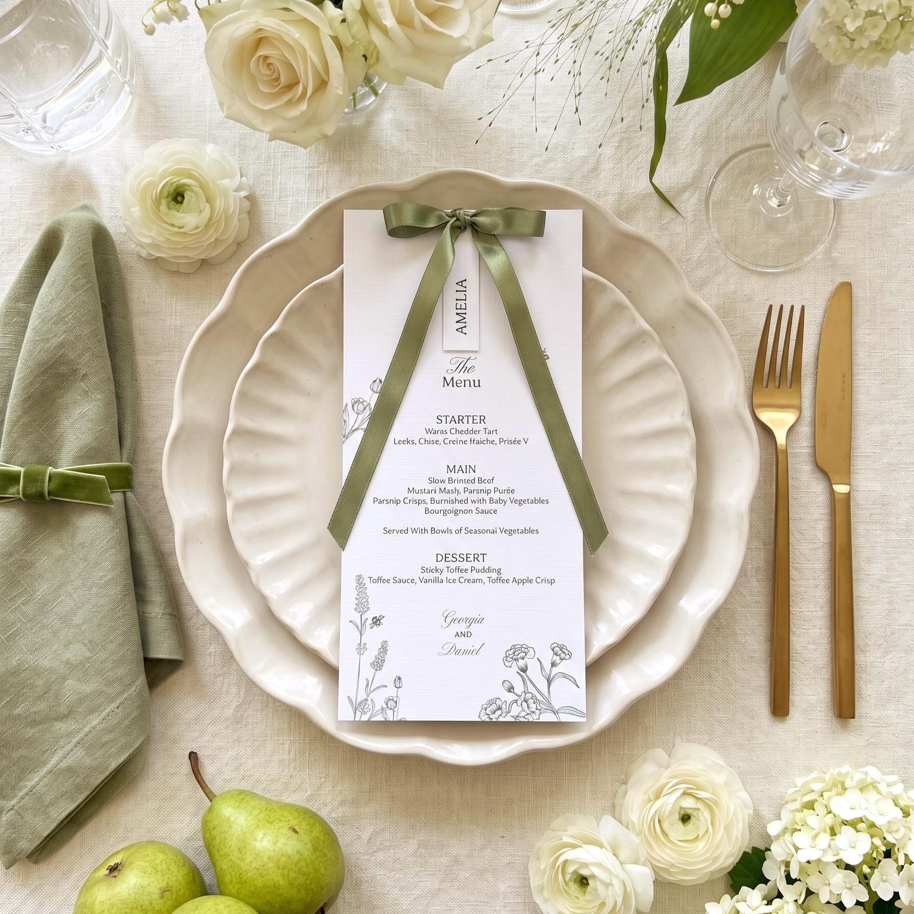 Olive green botanical wedding menu for Georgia and Daniel with an Amelia name tag on an olive satin bow, on scalloped cream plates, with a sage linen napkin tied with green velvet ribbon, gold cutlery, white ranunculus, ivory roses and green pears
